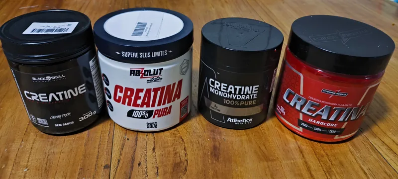 Quatro potes de creatina lado a lado sobre mesa de madeira: Black Skull, Absolut Nutrition, Atlhetica Nutrition e Integralmédica Hardcore